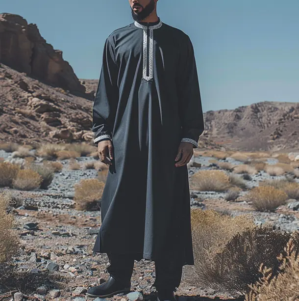 Man standing in the desert wearing a youthful navy blue thobe with white detailing.